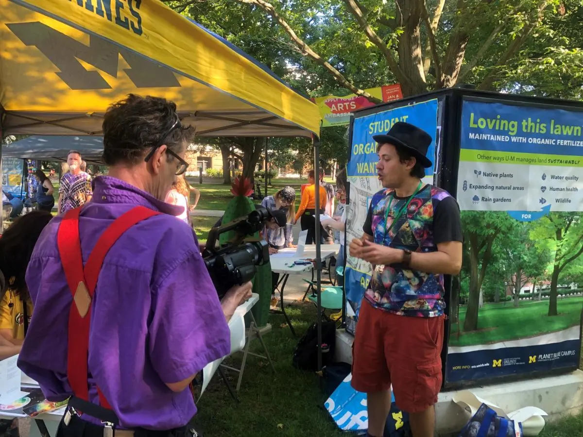 Two people talk beside an information tent on the campus lawn.